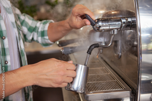 Cropped shot of unrecognizable male barista steaming milk for delicious cappuccino. Professional barista preparing coffee for a customer, using coffee machine
