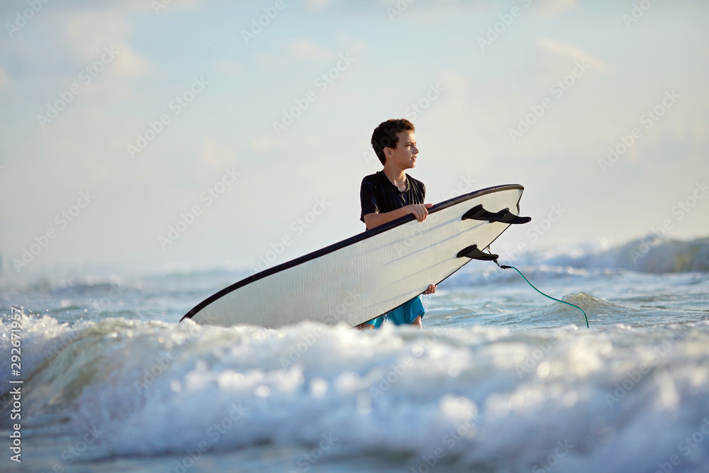 Naklejka premium Confident boy knee-deep in water with a surfboard