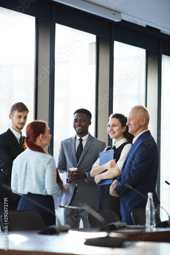 Diverse group of cheerful business people talking actively while standing by window in conference room