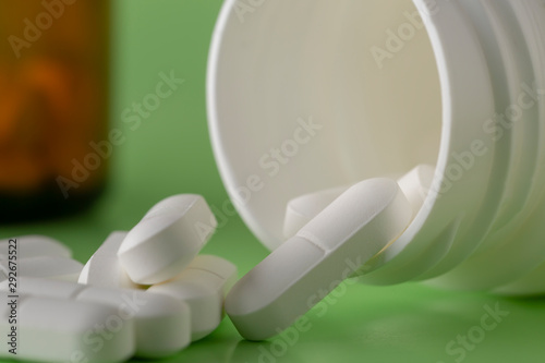 Glass and plastic medicine bottles and scattered white drugs on a green background
