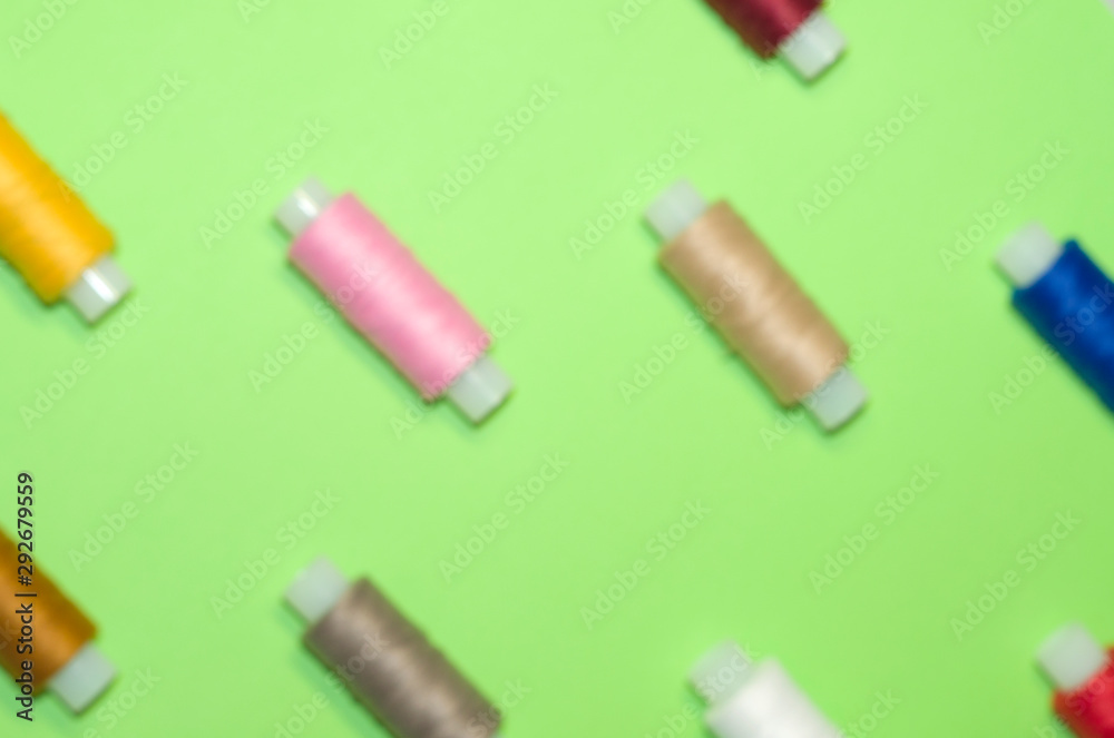 needlework, craft, sewing and tailoring concept - row of colorful thread spools on green background, flat lay, top view
