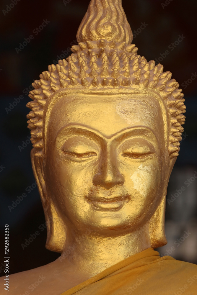 Close up of the face of a golden Buddha sculpture adorned in an orange robe against a black background