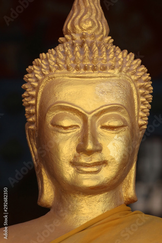 Close up of the face of a golden Buddha sculpture adorned in an orange robe against a black background