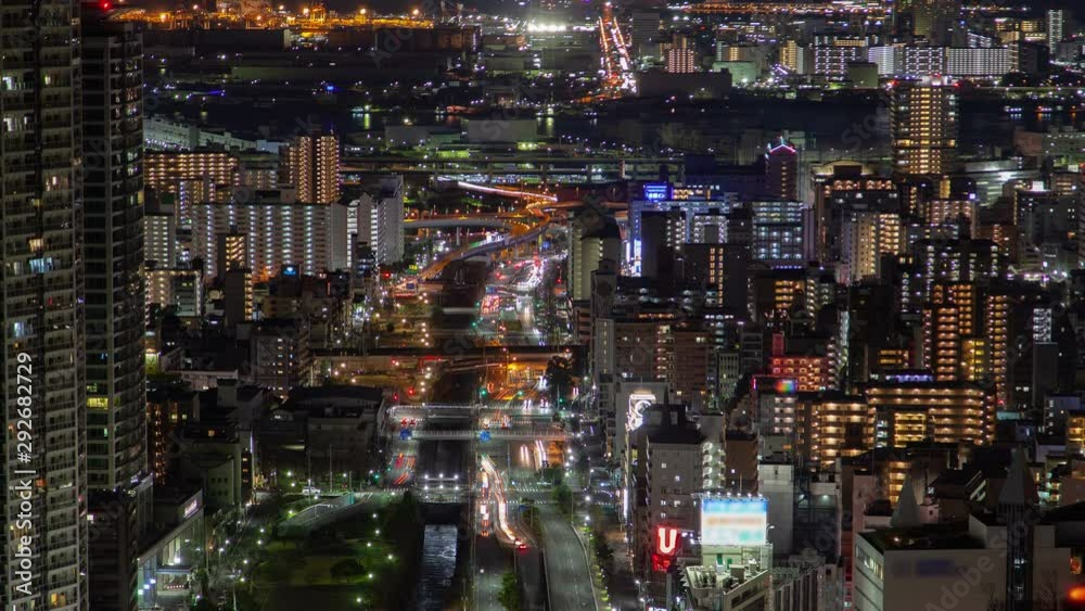 Timelapse zoom out Kobe city upper view on street main multi-lane highway with busy urban traffic at night rush hour among highrise illuminated buildings and skyscrapers against distant seaport Timelapse zoom out Kobe city upper view on street main multi-lane highway with busy urban traffic at night rush hour among highrise illuminated buildings and skyscrapers against distant seaport