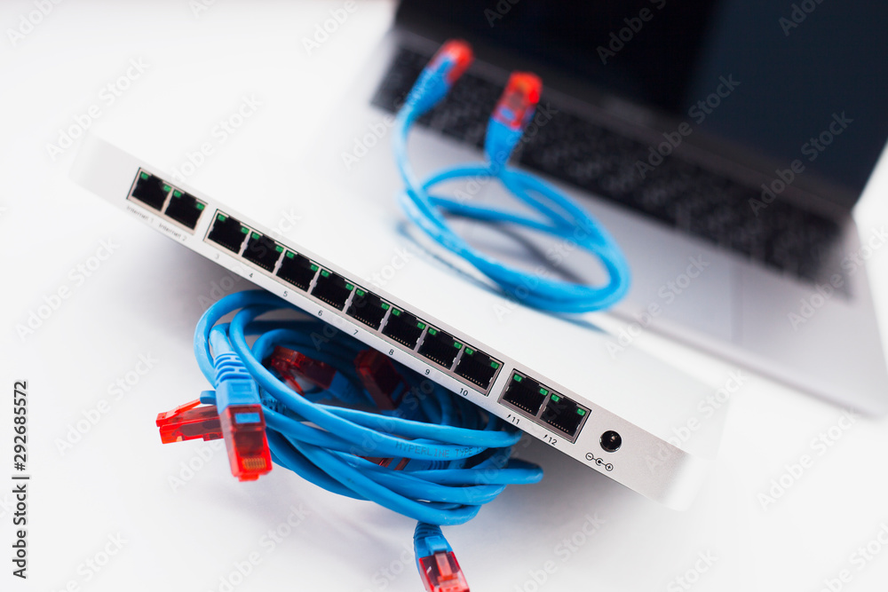 Smart office concept. Silver switch and new laptop on the white background. Network configuration process. Space for your text. Closeup. Smart office concept. Silver switch and new laptop on the white background. Network configuration process. Space for your text. Closeup.