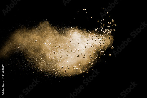 Fototapeta Split debris of brown stone exploding with brown powder against black background