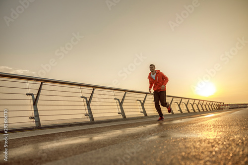 Purposeful young sportsman jogging on a bridge
