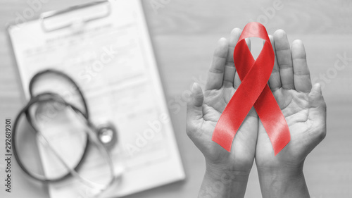 World aids day and national HIV/AIDS and ageing awareness month with red ribbon on woman hand support (bow isolated with clipping path) photo
