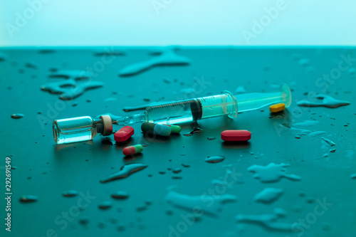 Dialed syringe with a medicinal product lying among drops of water and medicines on a blue background. The concept of pharmacology.