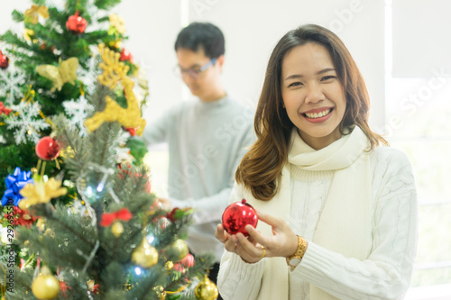 close up young beautiful asian woman smiling with happiness feeling and holding red baubles ball to decorate on fir tree at living room with friends for party celebration of merry christmas festival t photo