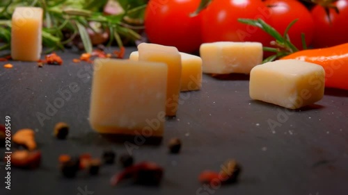 Hard cheese cubes fall on a black surface with spices and tomatoes photo