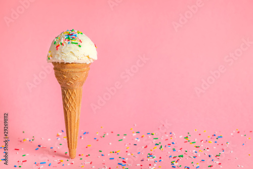 vanilla flavor ice cream in waffle cone with strewed multicolor sprinkles on pink background