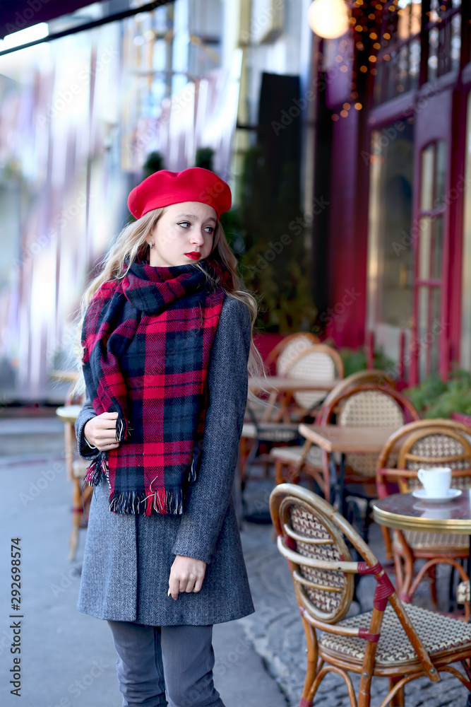 Fototapeta premium young girl in a red beret and a gray coat near a cafe
