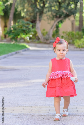 portrait of little girl in red dress walking in the park