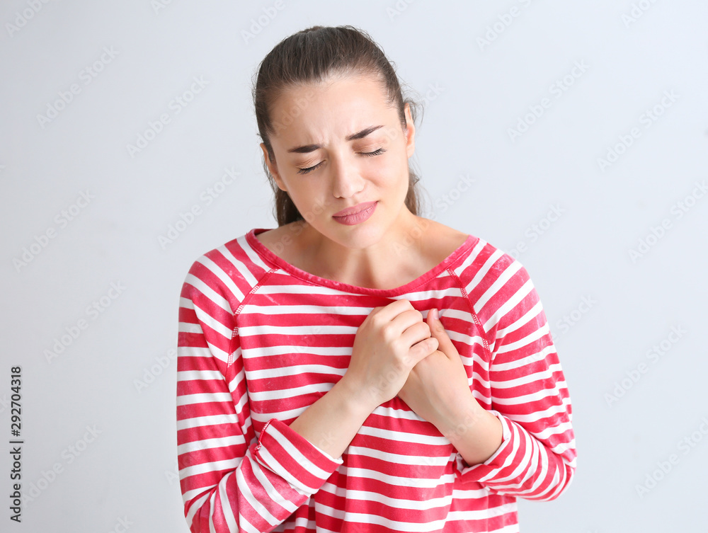 Young woman suffering from heart attack on light background