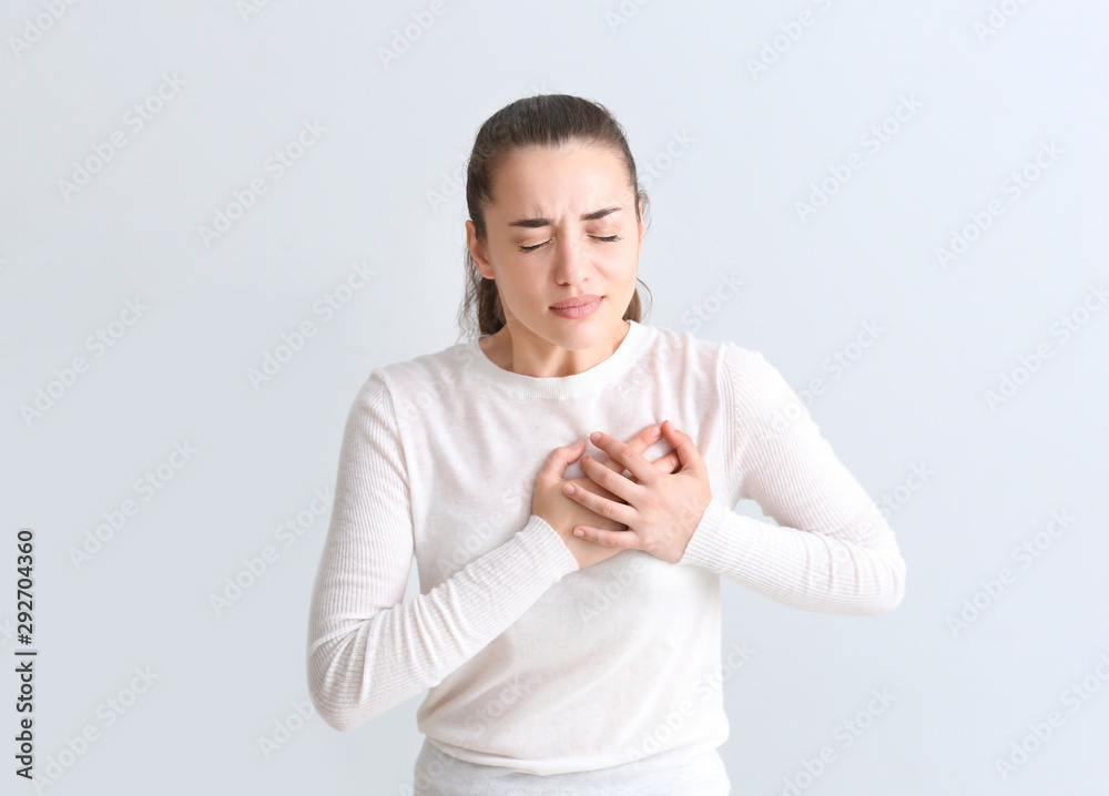 Young woman suffering from heart attack on light background Young woman suffering from heart attack on light background