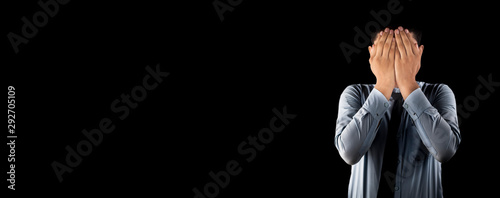 Embarrassed business employee worker wearing a corporate blue shirt with black necktie isolated on black background covering his face with his hands. Wide-angle shot.