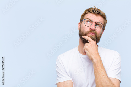 young blonde adult man thinking, feeling doubtful and confused, with different options, wondering which decision to make photo