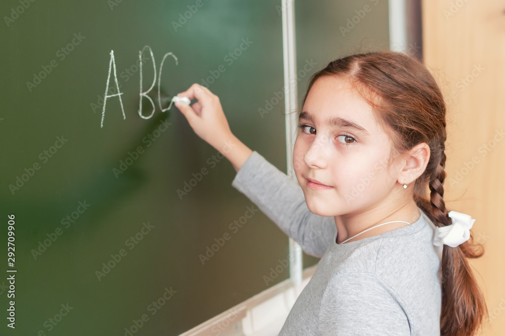Elementary school girl stands in front of a blackboard and writes with chalk