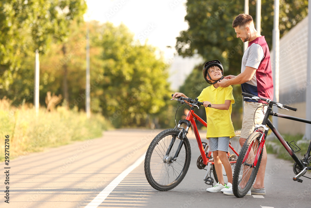 Father helping his son to put on bicycle helmet outdoors Father helping his son to put on bicycle helmet outdoors