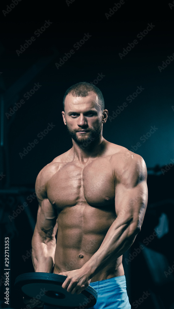 Obraz premium Strong athletic sportsman doing exercises with weightlifting plate in gym