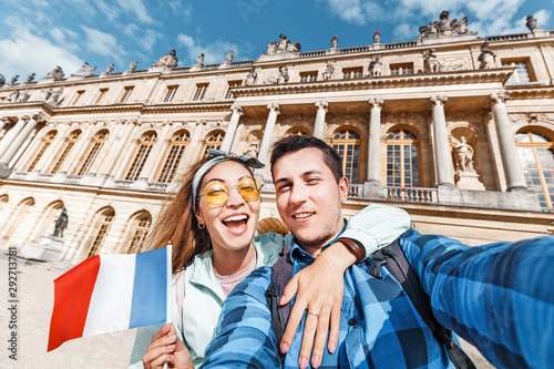 A couple in love, an Asian girl and a European man embrace and take a selfie against the backdrop of the Royal Palace of Versailles in France. Travel and honeymoon