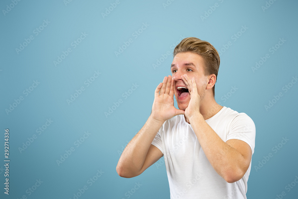 Caucasian young man's half-length portrait on blue studio background. Beautiful male model in shirt. Concept of human emotions, facial expression, sales, ad. Calling somebody, happy. Caucasian young man's half-length portrait on blue studio background. Beautiful male model in shirt. Concept of human emotions, facial expression, sales, ad. Calling somebody, happy.