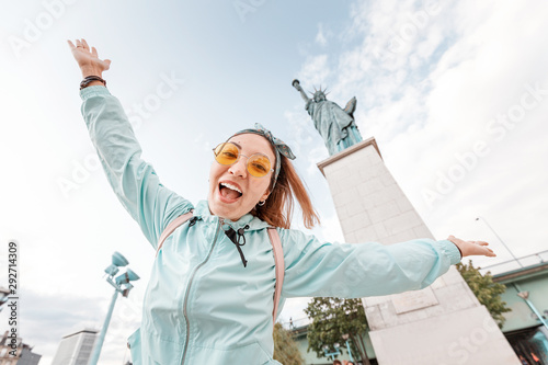 Happy Asian girl traveler funny posing on the background of the famous Statue of Liberty. The concept of tourism and immigration