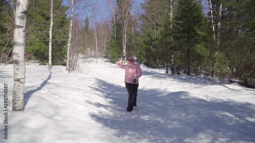 A cheerful pensioner cheerfully plays snowballs on the street on a warm winter day. Grandma is enjoying life.
