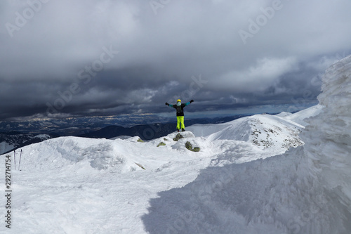 Skier-athlete stands on the edge of a high cliff against High Tatras and approaching thunderstorm. Enjoys view to the valley and experiencing a wave of joy for a successful climb © Fauren