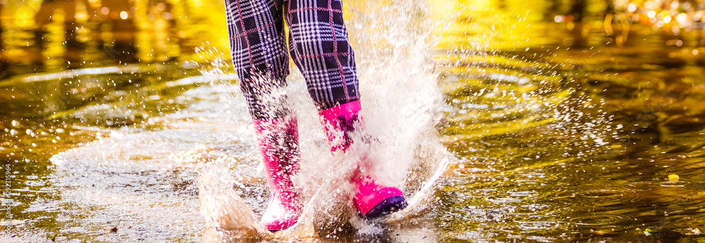 Feet of child in pink rubber boots jumping over a puddle in the rain ...