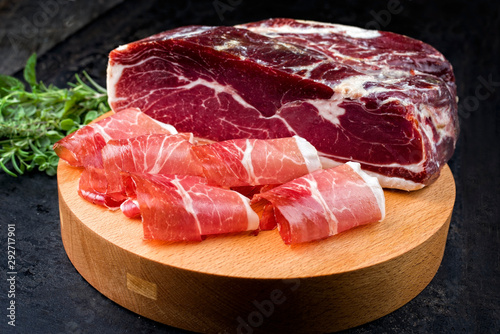 Traditional dry cured and smoked ham with a bouquet garni offered as closeup on a modern design cutting board photo