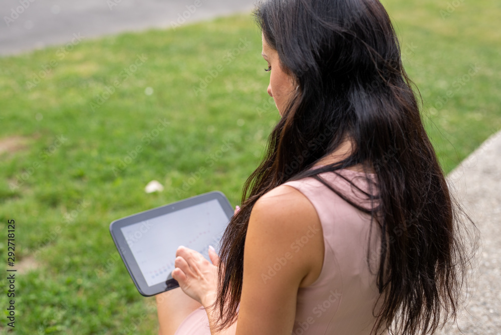 Business woman in the park works with the tablet-PC. Mobile working outside the office. Smart working of a young woman in the park. View over her shoulder at the tablet-PC Business woman in the park works with the tablet-PC. Mobile working outside the office. Smart working of a young woman in the park. View over her shoulder at the tablet-PC