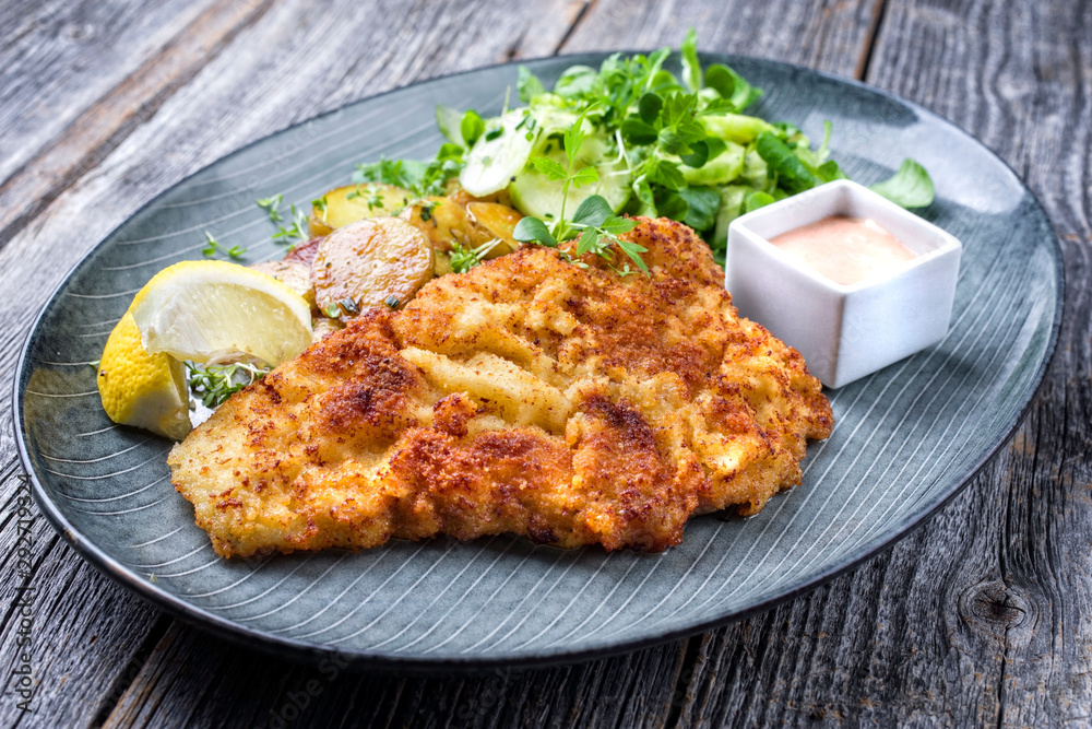Deep fried Wiener schnitzel from veal topside with fried potatoes and lettuce as closeup modern design plate Deep fried Wiener schnitzel from veal topside with fried potatoes and lettuce as closeup modern design plate