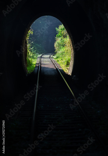 View from the railway tunnel in the mountains to the tropical jungle vegetation and sunlight. In the background  the beginning of the next tunnel is visible in the haze.