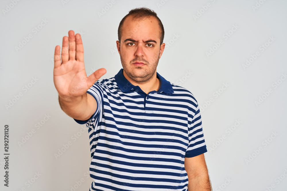 Young man wearing casual striped polo standing over isolated white background doing stop sing with palm of the hand. Warning expression with negative and serious gesture on the face. Young man wearing casual striped polo standing over isolated white background doing stop sing with palm of the hand. Warning expression with negative and serious gesture on the face.