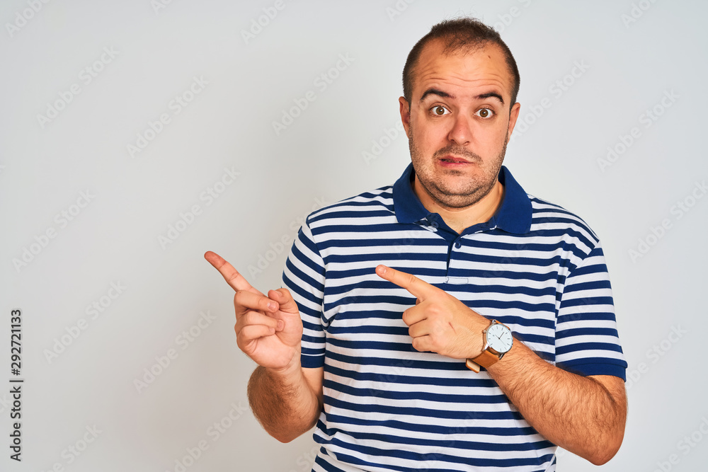 Young man wearing casual striped polo standing over isolated white background Pointing aside worried and nervous with both hands, concerned and surprised expression Young man wearing casual striped polo standing over isolated white background Pointing aside worried and nervous with both hands, concerned and surprised expression