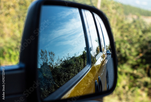 View of the road from the rearview mirror of a yellow car.