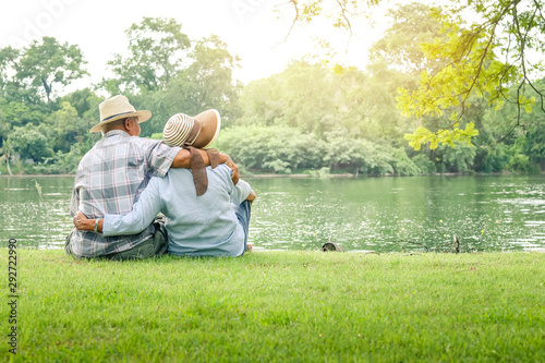 An elderly couple hugging each other with love and happiness in a park with a large pond. Senior community concept, good health, longevity
