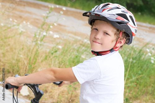 Back view of small boy in protective helmet riding bicycle in park on summer day. Weekend activity.