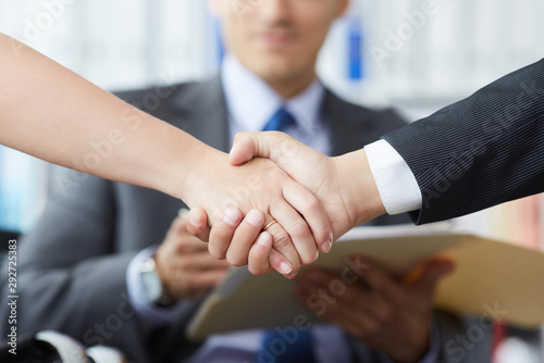 Business people shaking hands, finishing up a meeting. Male and female hands in handshake closeup with male colleague in background.