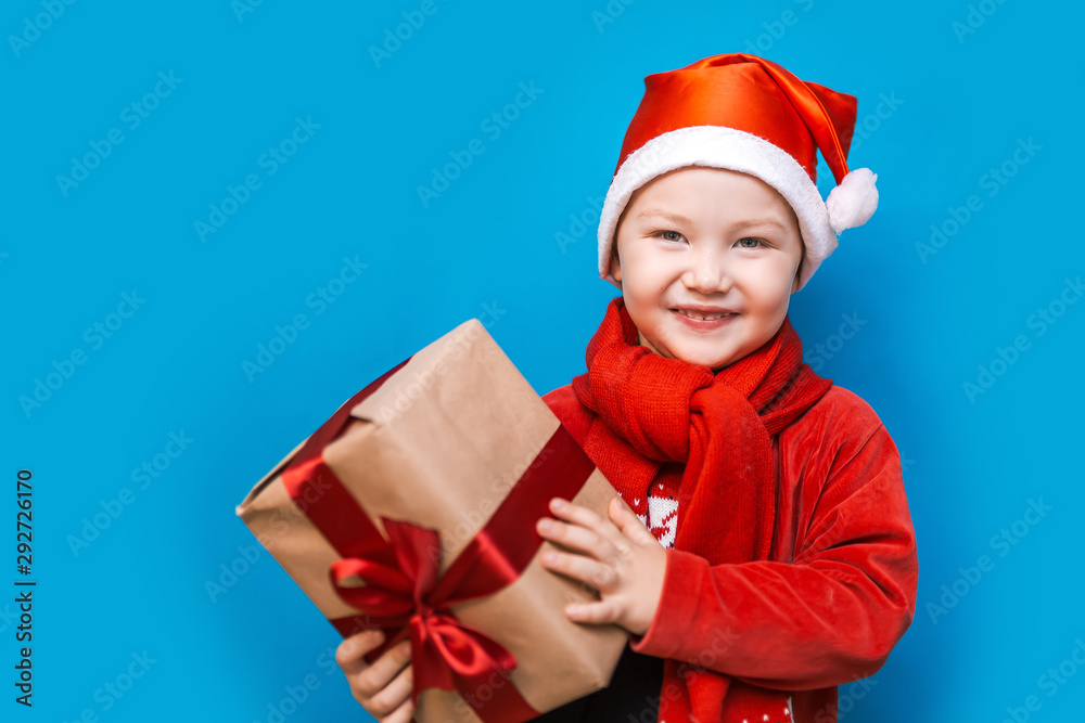 portrait of a happy little boy holding a new christmas gift with red ribbon in red clothes. happy new year, merry christmas portrait of a happy little boy holding a new christmas gift with red ribbon in red clothes. happy new year, merry christmas