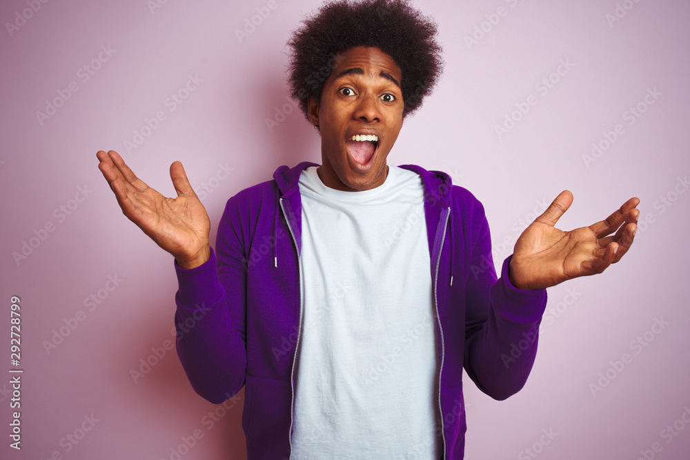 Young african american man wearing purple sweatshirt standing over isolated pink background celebrating crazy and amazed for success with arms raised and open eyes screaming excited. Winner concept Young african american man wearing purple sweatshirt standing over isolated pink background celebrating crazy and amazed for success with arms raised and open eyes screaming excited. Winner concept