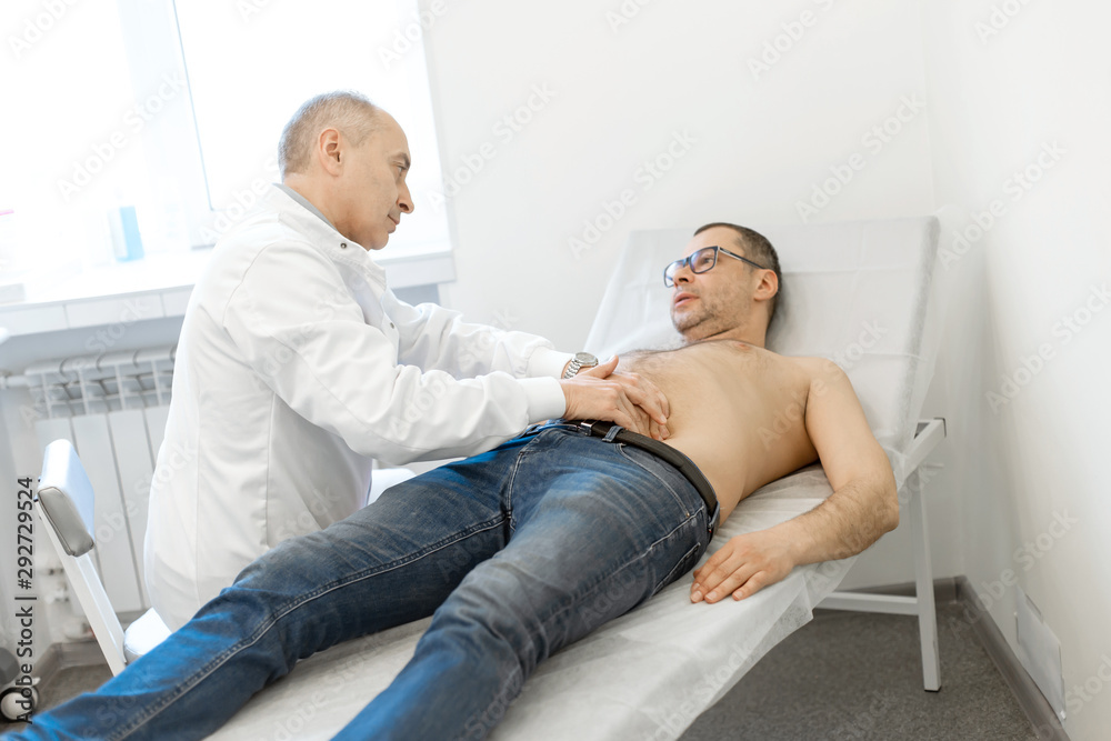 Obraz premium Doctor therapist probes the stomach of a male patient who is lying on a couch. Professional medical advice