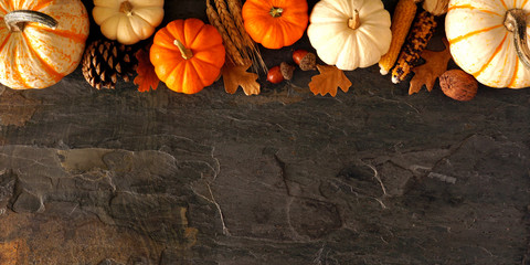 Fall top border banner of pumpkins and autumn decor on a dark stone background with copy space