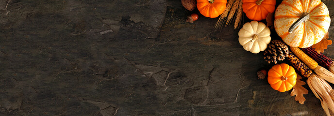 Fall corner border banner of pumpkins and autumn decor on a dark stone background with copy space