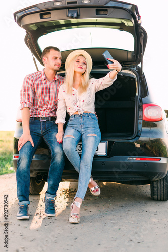 Young couple sitting together in the car trunk and taking selfie photo on the roadside in the forest. © F8  \ Suport Ukraine