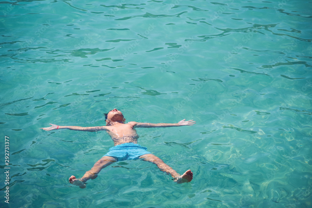 Healthy lifestyle. European boy in blue swim shorts swimming in blue clear sea water during his trip to Spain.