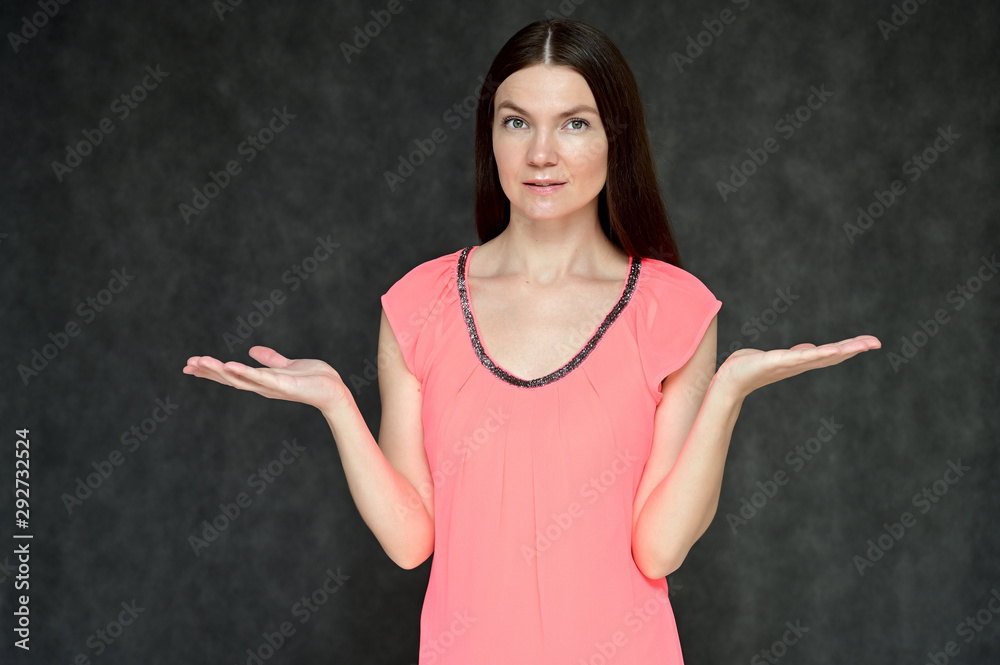 Portrait of a pretty young brunette woman with combed hair on a gray background in a pink blouse. It is in different poses. Looks straight at the camera. Slim figure. Portrait of a pretty young brunette woman with combed hair on a gray background in a pink blouse. It is in different poses. Looks straight at the camera. Slim figure.