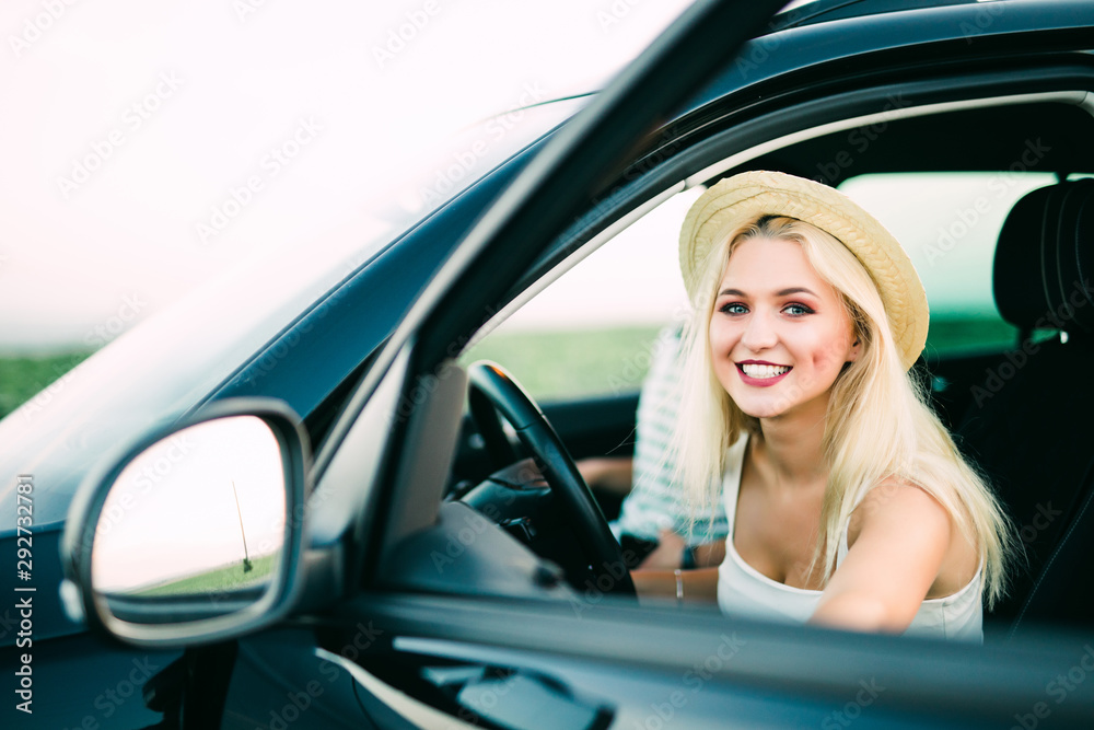 Attractive woman is ready to drive her car opening the door and staying behind it. The girl is smiling and looking aside. Copy space in right side